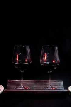 Two wine glasses filled on top of a tile, On a black background and utensils for wine