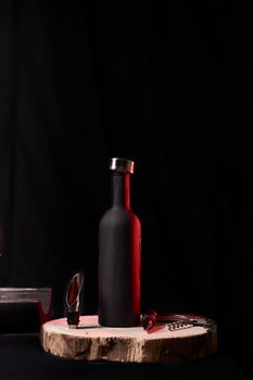 Bottle and wine utensils on wooden stump, on black background