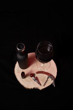 Glass, bottle and utensils for wine, on black background and wooden stump
