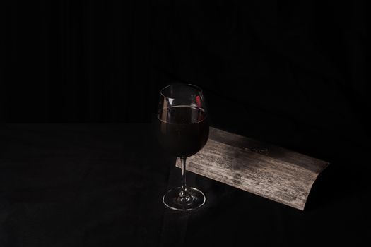 Glass of red wine, next to a tile, on black background