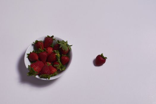 Bowl of ripe strawberries with one outside. Colors of nature