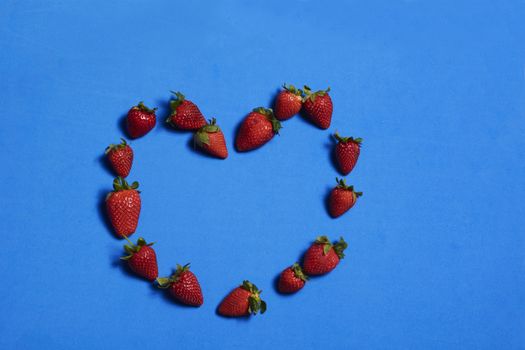 Heart made of strawberries on blue background. Colors of nature