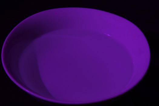 White bowl full of water on black background, calm water, violet color