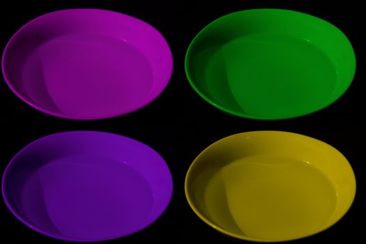 Four bowls with water of different colors, magenta, yellow, purple and green, black background, complementary colors