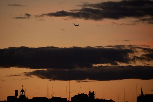 Airplane at sunset crossing the clouds in the city. City silhouettes