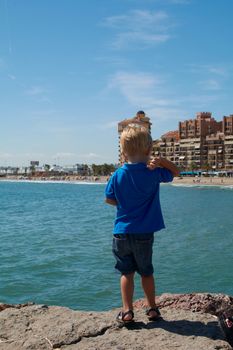 Blond boy playing on a sunny day at the beach. Mediterranean colors