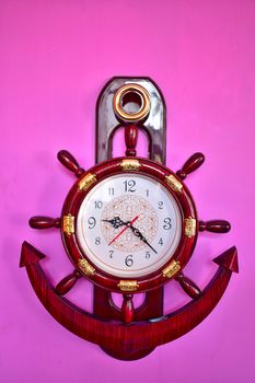 A well designed ship wheel and anchor wall clock hanging on pink wall