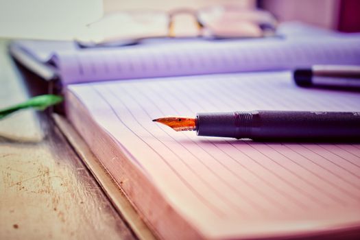 An old fountain pen on a blank page of a diary. The cap of the pen and spectacles are behind the pen.