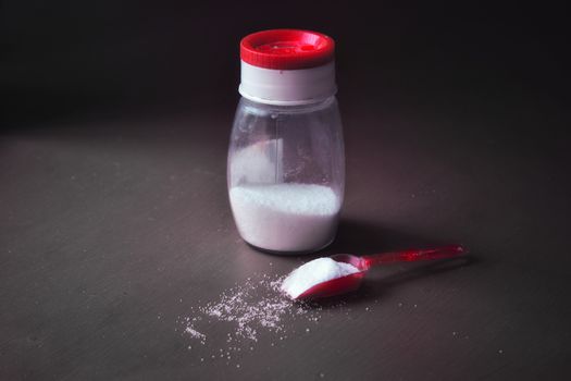 Spoon full of salt with scattered salt on the ground and a salt container with red cap
