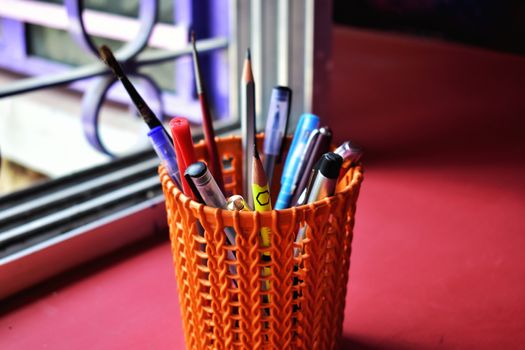 An orange colored pen case with many types of pens and pencils and some paint brush