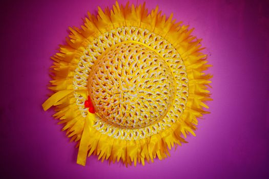 A round beautifully designed yellow colored hat hanging on a purple colored wall