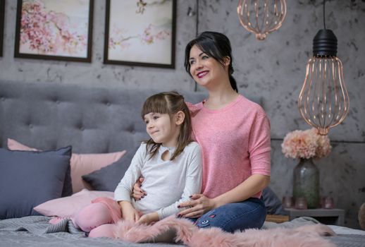 Family mother and child daughter play and hug in bed