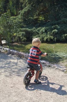 Blond boy playing in the park with his bicycle, Colors of summer