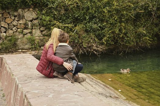 Mother and son watching the water raft with ducks. Colors of nature