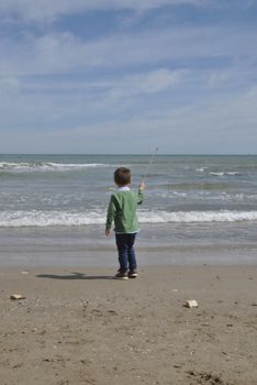Boy in green clothes looking at the sea, Playing with a stick