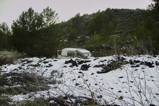 Old abandoned car in snow landscape, surrounded by trees and storm sky