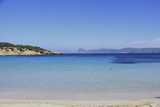 Deserted beach with turquoise waters, bright day, Mountains in the background and bright blue day