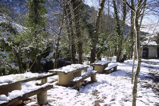Recreation area in snowy mountain in winter. Tables and chairs full of snow surrounded by trees