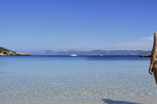 Deserted beach with turquoise waters, bright day, Mountains in the background and bright blue day, woman looking at the sea