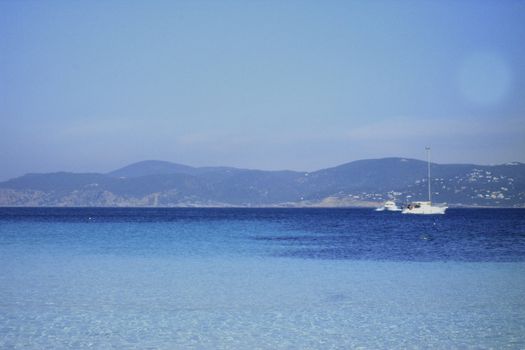 Deserted beach with turquoise waters, bright day, Mountains in the background and bright blue day, two boats sailing