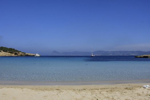 Deserted beach with turquoise waters, bright day, Mountains in the background and bright blue day, two boats sailing