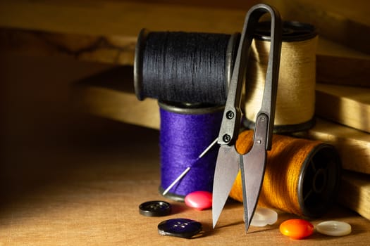 Needle and threads against plastic button and thread cutting scissors on wooden table. Close Up and copy space for text. Concept of tailor or Designer.