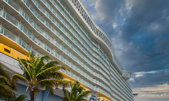 Rows of balconies on a large luxury cruise ship docked at a tropical port