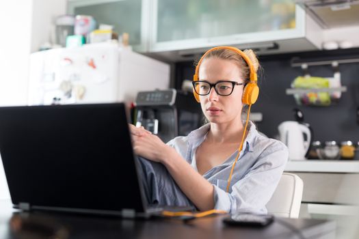 Female freelancer in her casual home clothing working remotly from her dining table in the morning. Home kitchen in the background. Stay healthy and stay at home during corona virus pandemic.