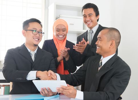 Group of Malaysian businesspeople having deals on desk inside office room, businesspeople clapping hands.