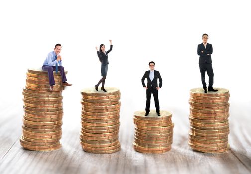 Miniature business people sitting and standing on stack of coins.