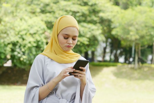 Muslim woman looking at mobile phone, negative emotions, phishing scams concept.