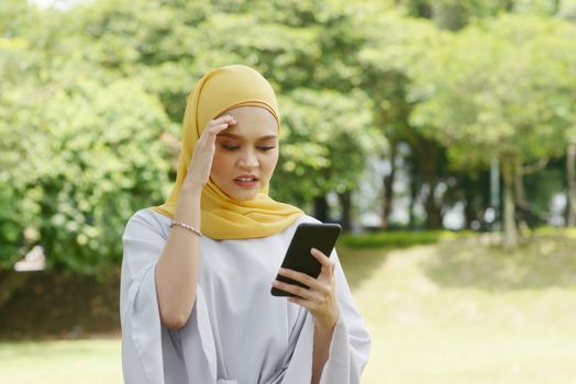 Muslim woman looking at mobile phone, negative emotions, phishing scams concept.