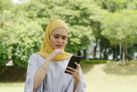 Muslim woman looking at mobile phone, negative emotions, phishing scams concept.