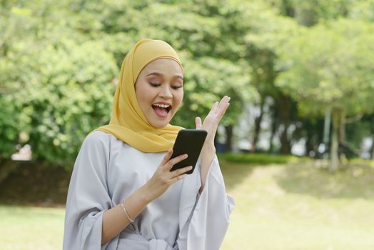 Portrait of cheerful Muslim girl using smartphone, smiling at outdoor.