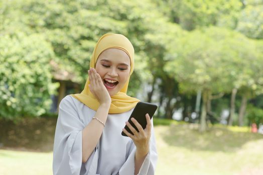 Portrait of cheerful Muslim girl using smartphone, smiling at outdoor.