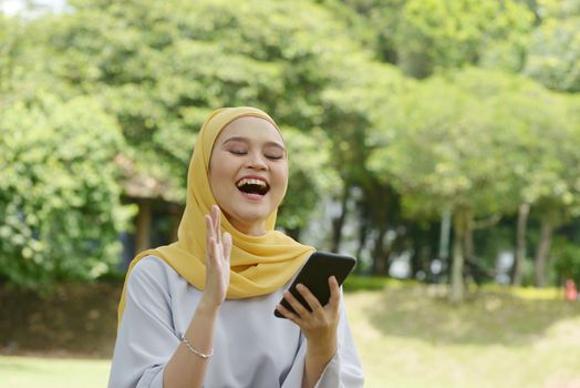 Portrait of cheerful Muslim girl using smartphone, smiling at outdoor.