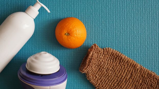 Lotion, orange, shower sponge and anti-cellulite massager on a blue background. Healthy and beautiful skin concept.