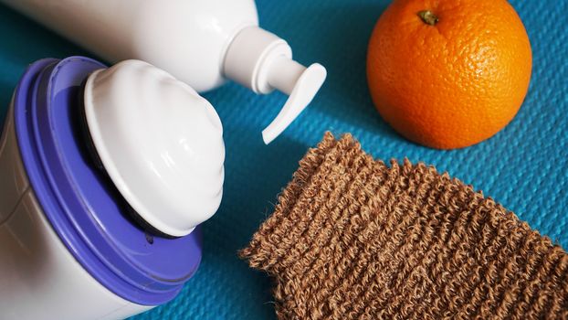 Lotion, orange, shower sponge and anti-cellulite massager on a blue background. Healthy and beautiful skin concept.