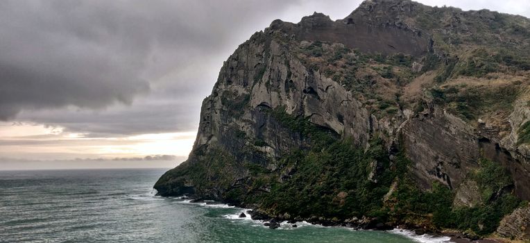 Cliff with green grass on the sea shore on a rainy cloudy day