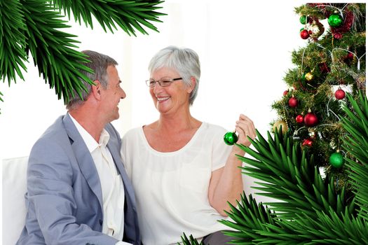 Mature couple sitting on sofa with a Christmas tree against digitally generated fir tree branches