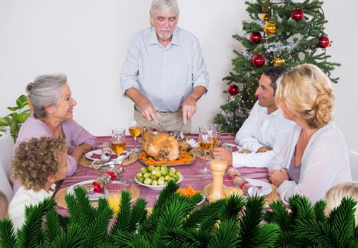 Composite image of grandfather carving the turkey against digitally generated fir tree branches