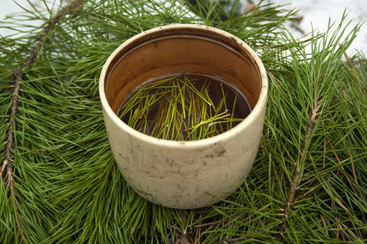 Cup of black tea with pine tree needles in it on green needles background side view. Healthy beverage tea in old cup.