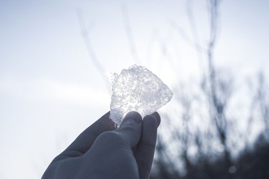 Piece of ice in man's hand close up against the sun. Look at the sun through the ice