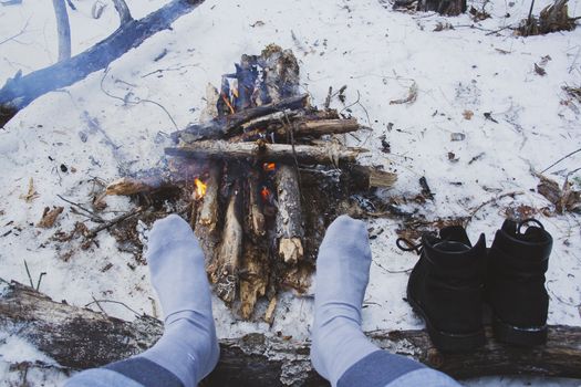 Man's legs against the bonfire in the forest. Bushcraft symbol. Solo survival in nature. Winter in the forest, travel