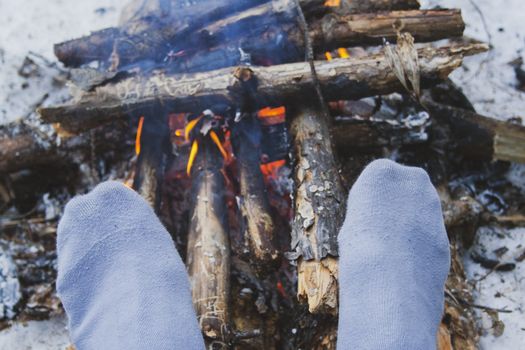 Man's legs against the bonfire in the forest. Bushcraft symbol. Solo survival in nature. Winter in the forest, travel