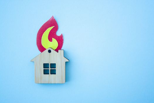 Fire house, insurance and mortgage concept. Small wooden house toy and paper fire shape on blue background top view with copy space