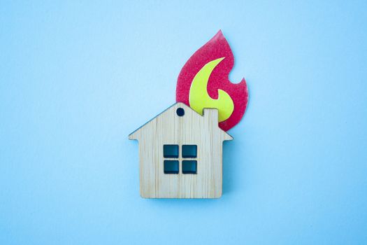 Fire house, insurance and mortgage concept. Small wooden house toy and paper fire shape on blue background top view 