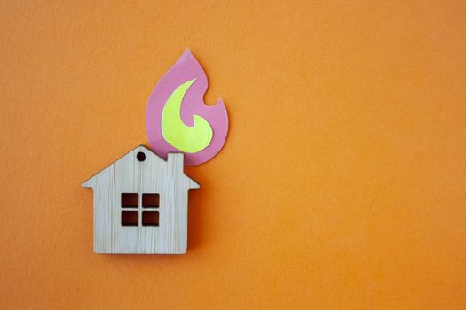 Fire house, insurance and mortgage concept. Small wooden house toy and paper fire shape on orange background top view with copy space