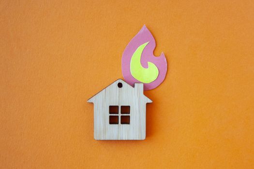 Fire house, insurance and mortgage concept. Small wooden house toy and paper fire shape on orange background top view