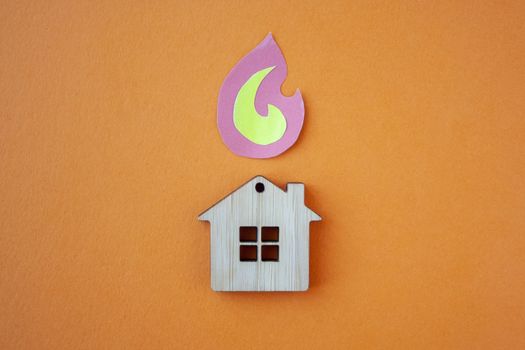 Fire house, insurance and mortgage concept. Small wooden house toy and paper fire shape on orange background top view 